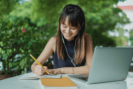 Person using laptop and taking notes in a notebook.