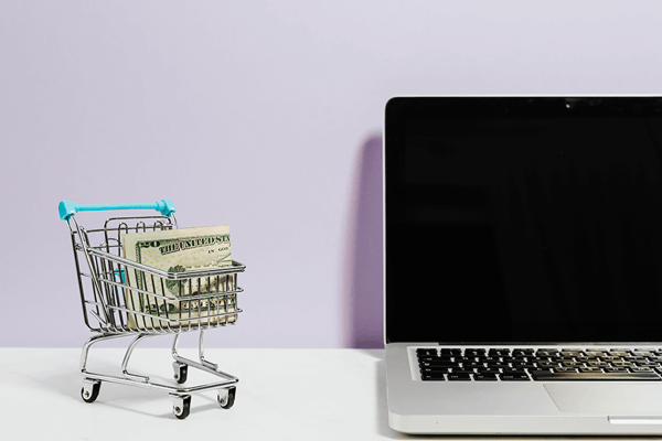 small shopping cart next to a laptop, representing online shopping